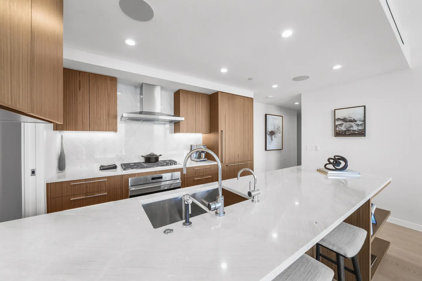 Bright kitchen with wood cabinets, stainless steel appliances, and a large white marble island with two gray stools.