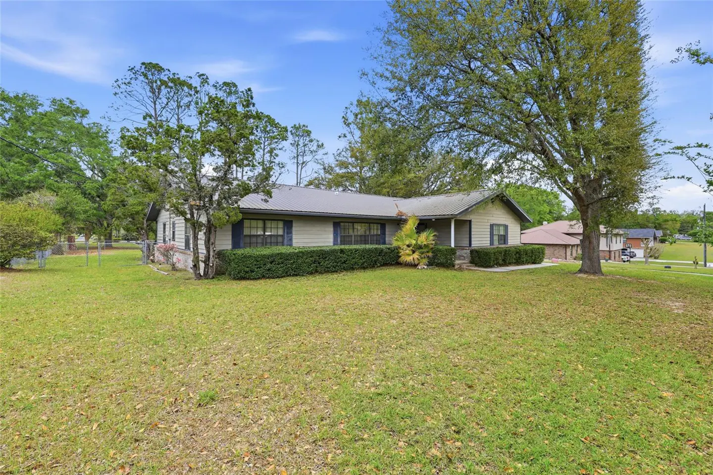 A single-story home with a gray metal roof, light siding, dark shutters, and green lawn.