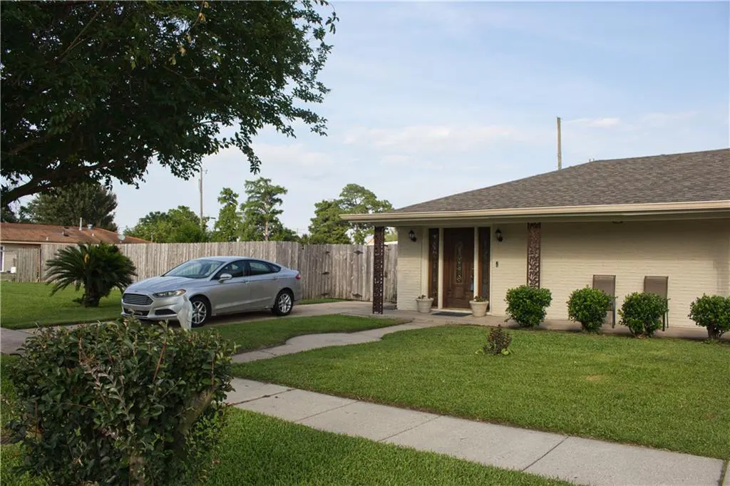 A single-story house with a silver car parked in the driveway. The house has a brown door and a well-manicured lawn.