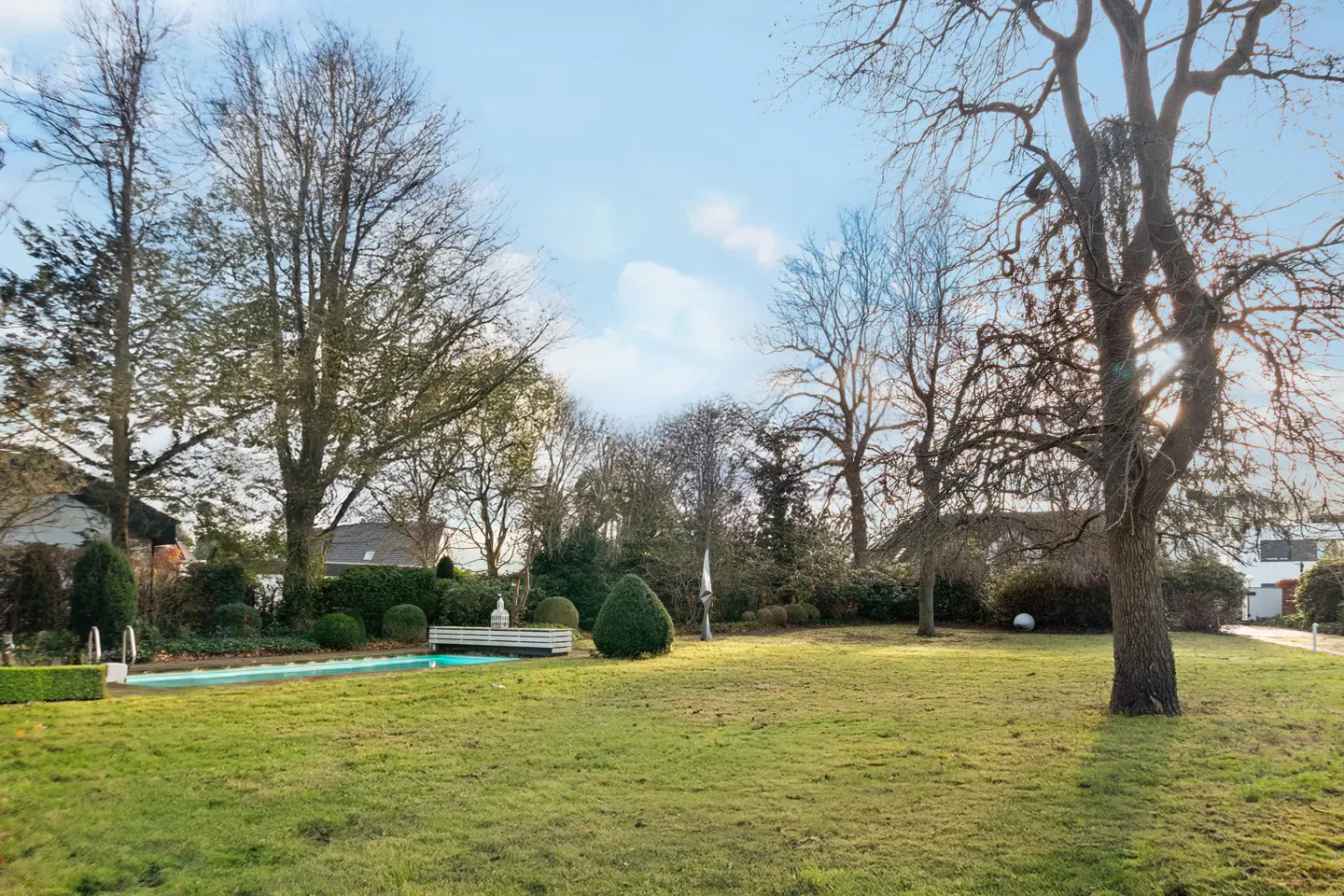 A backyard with a pool, green grass, and trees under a blue sky.