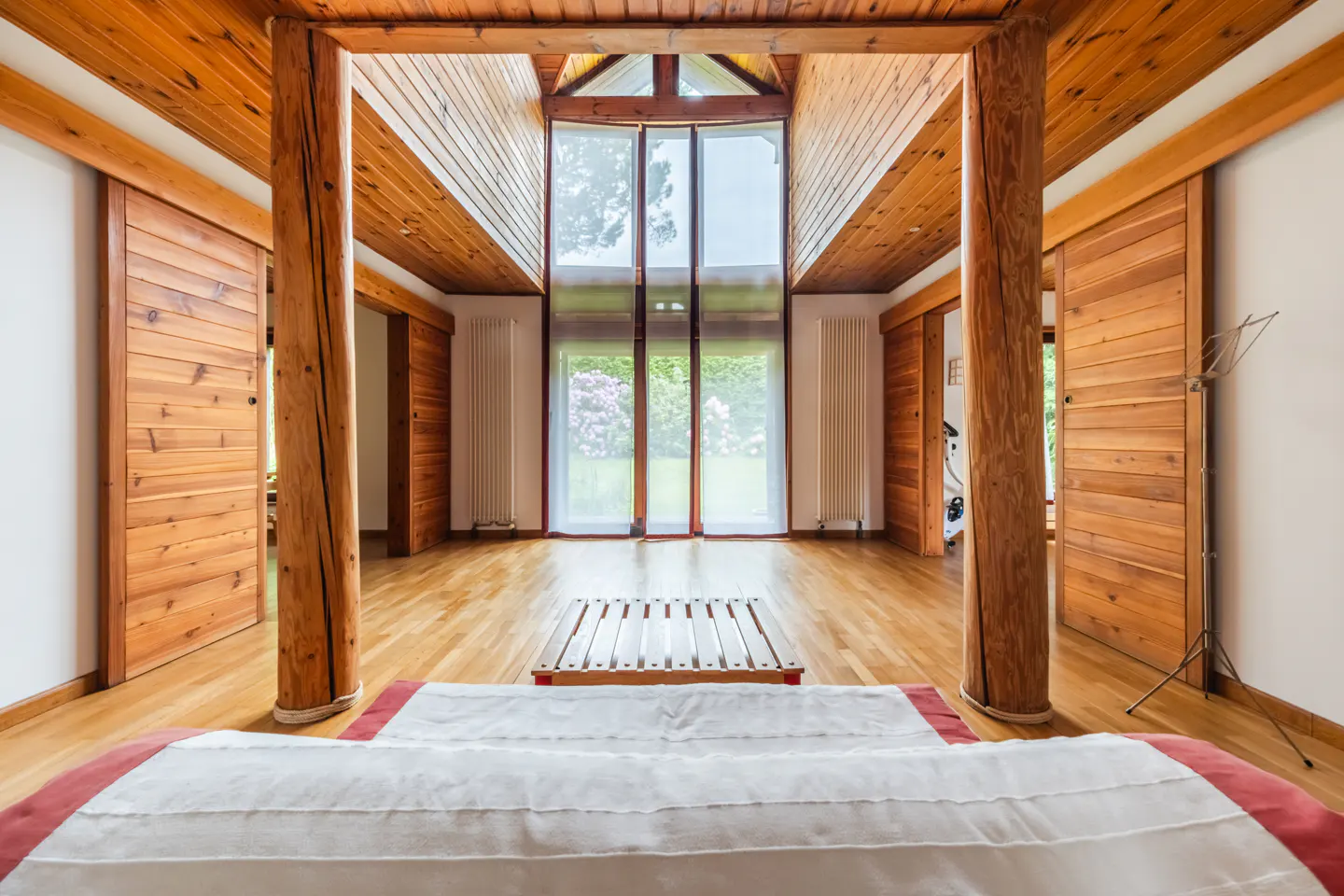 Interior view of a room with wood floors, walls, and ceiling, featuring large windows and sliding doors.