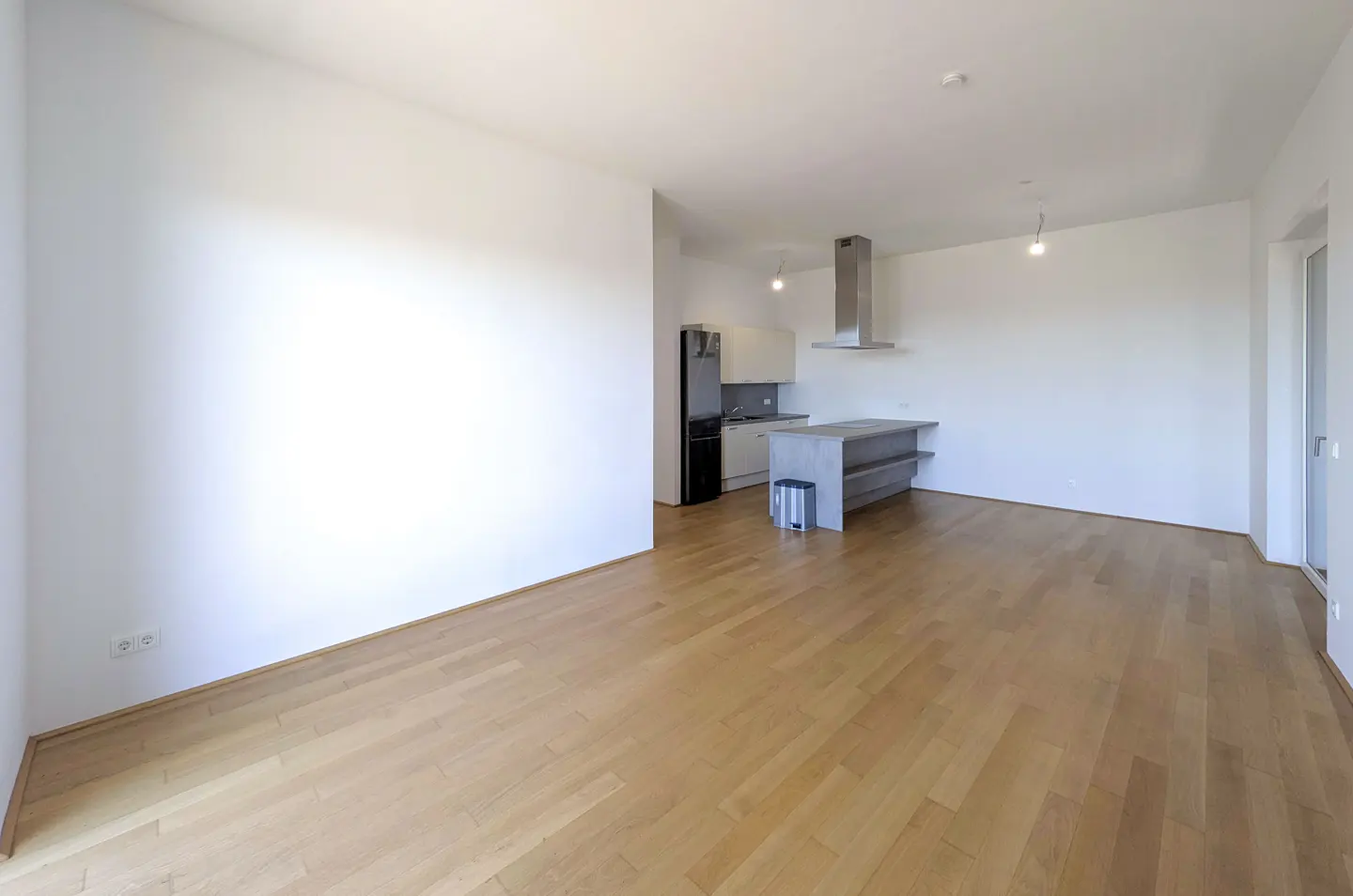 Modern open-plan living area with light wood floors, white walls, and a minimalist kitchen with a gray island.