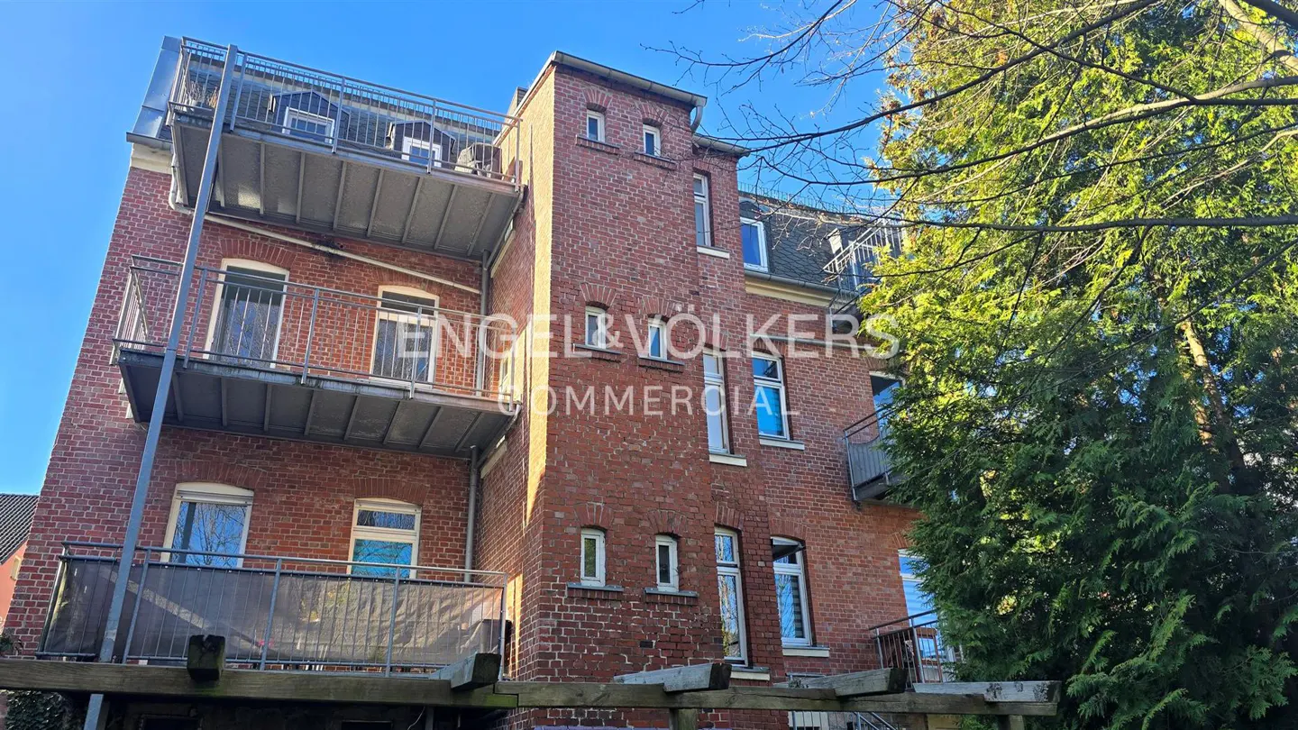 Exterior view of a red brick building with balconies and the Engel & Völkers Commercial logo.