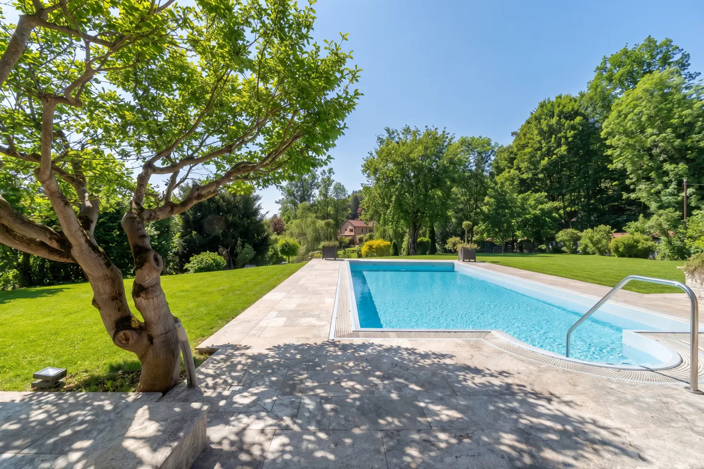 A bright blue swimming pool is surrounded by green grass and trees on a sunny day.