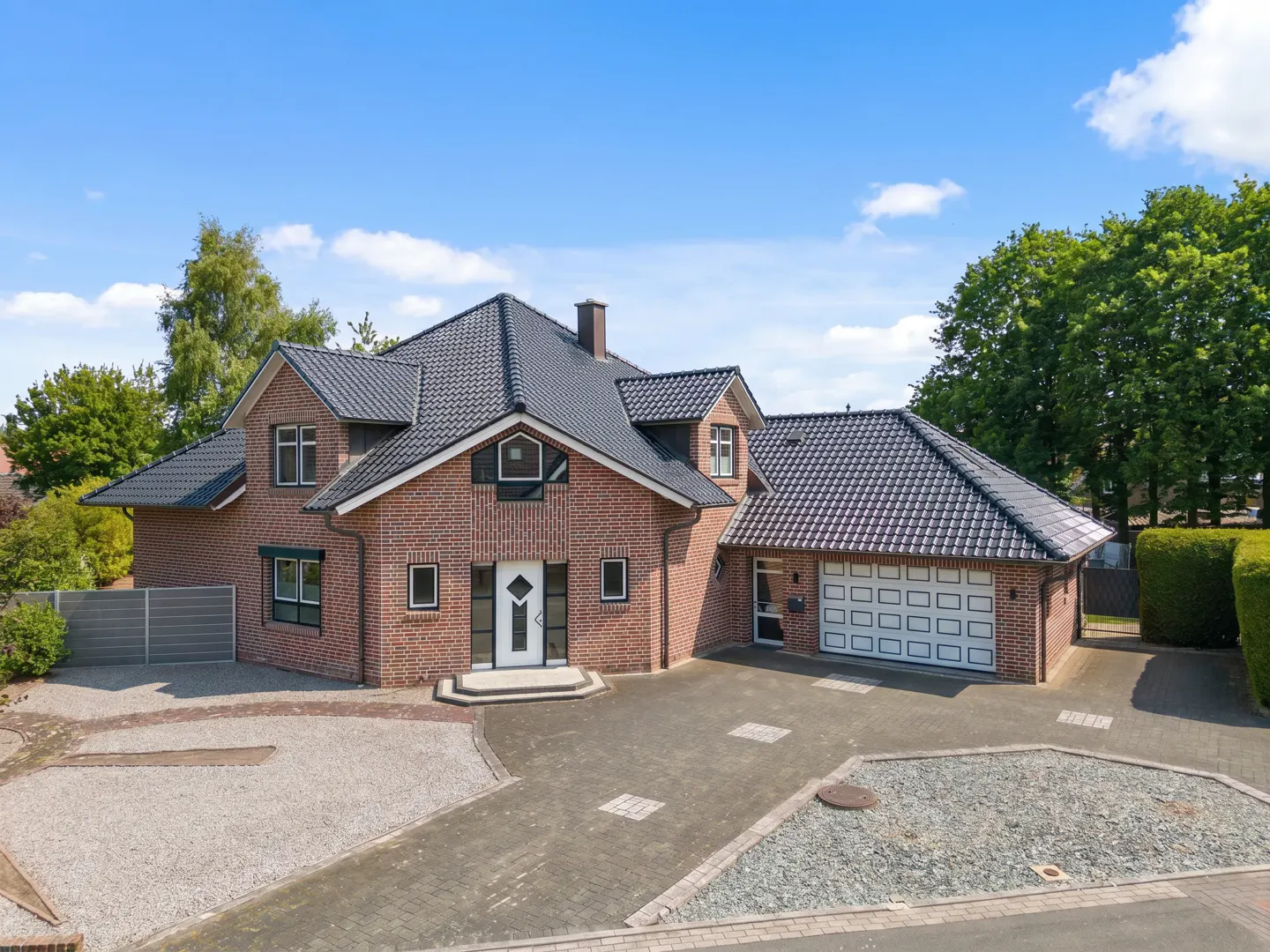 Two-story brick house with a black roof and white trim, a garage, and a paved driveway on a sunny day.