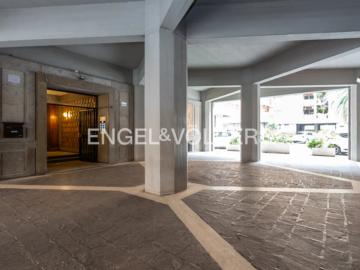 Covered parking area with stone floors and concrete pillars. An open elevator is visible in the background.