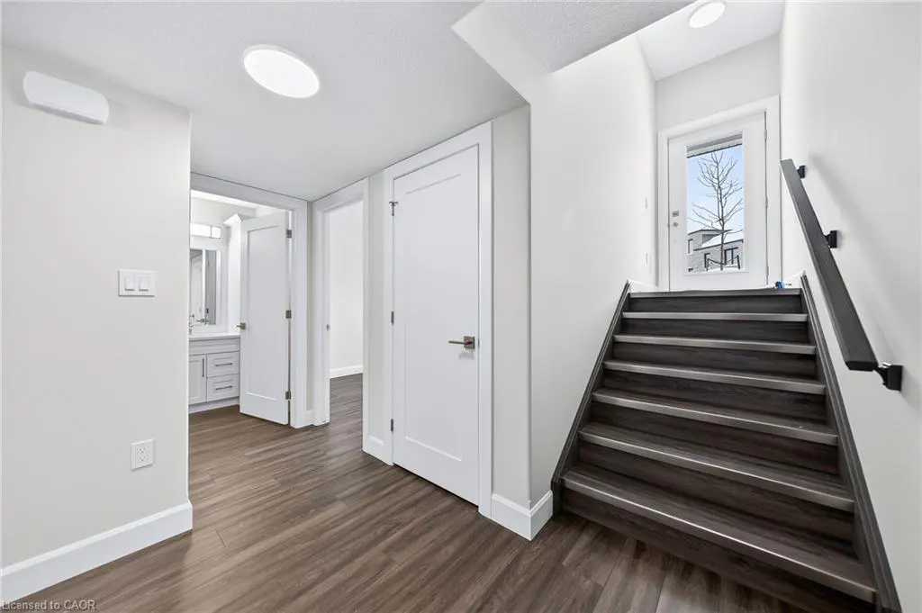 Interior view of a home's entryway with wood floors, white walls, stairs, and doors. A bathroom is visible in the background.