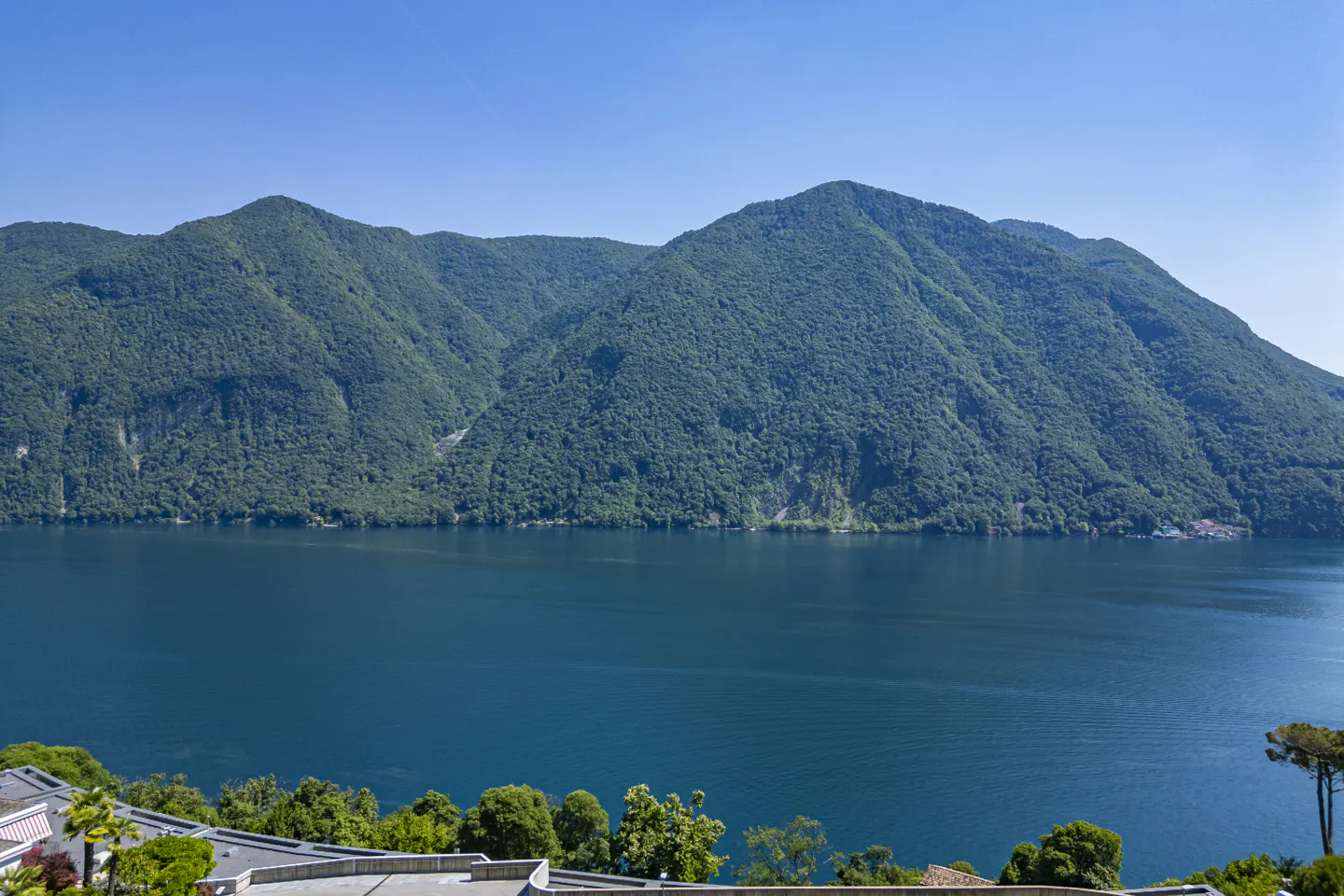 A scenic view of a deep blue lake framed by lush, green mountains under a clear, bright blue sky.