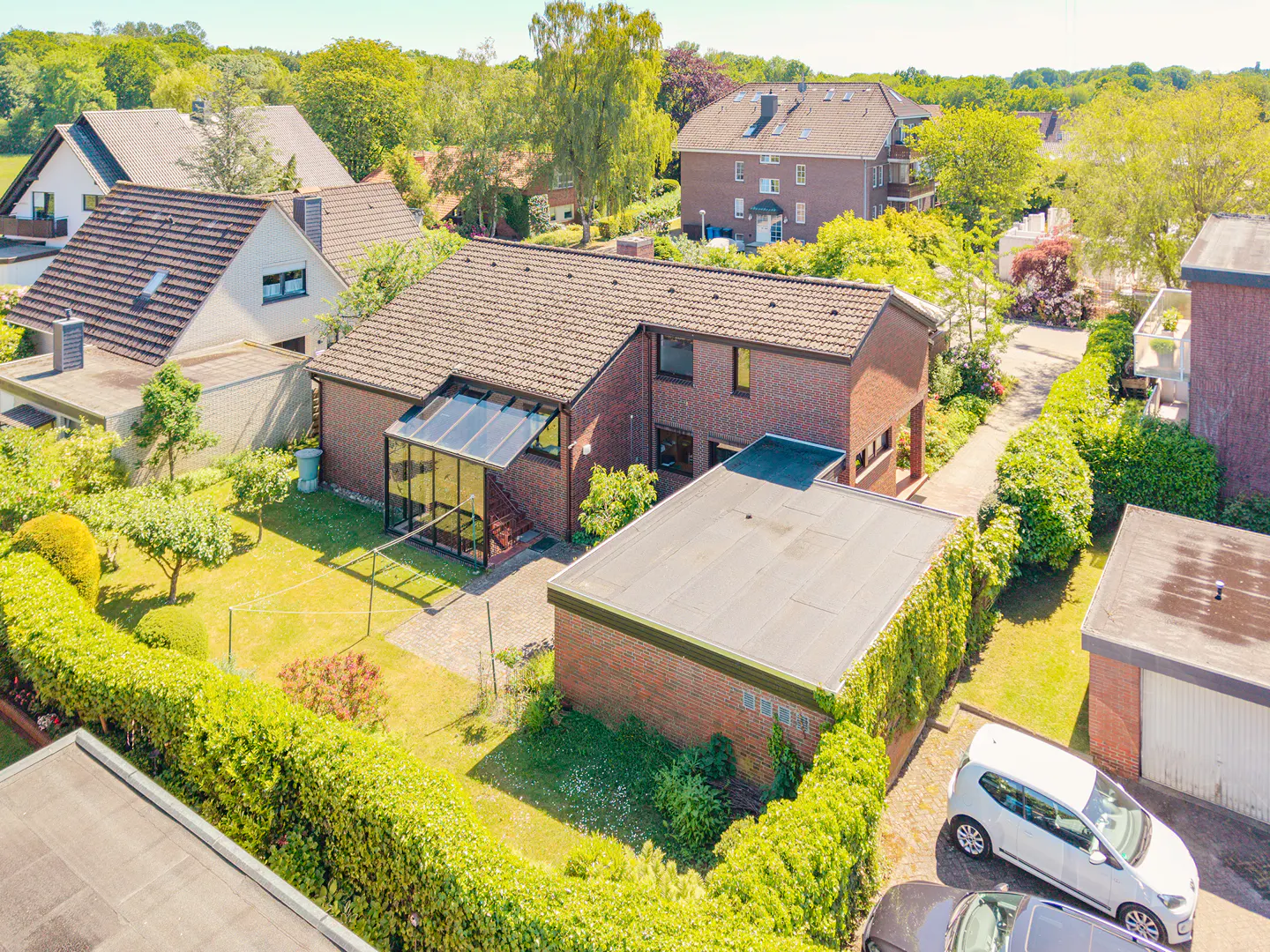 Aerial view of a red brick house with a glass conservatory, a flat-roofed garage, and a green garden in a suburban area.