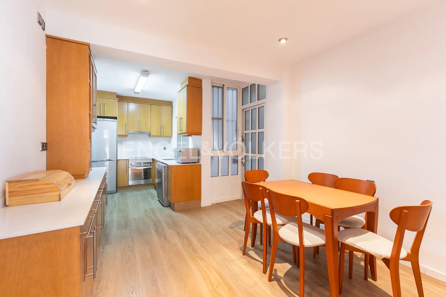 A bright, modern kitchen and dining area with wood cabinets, white walls, and a wooden table with six chairs.