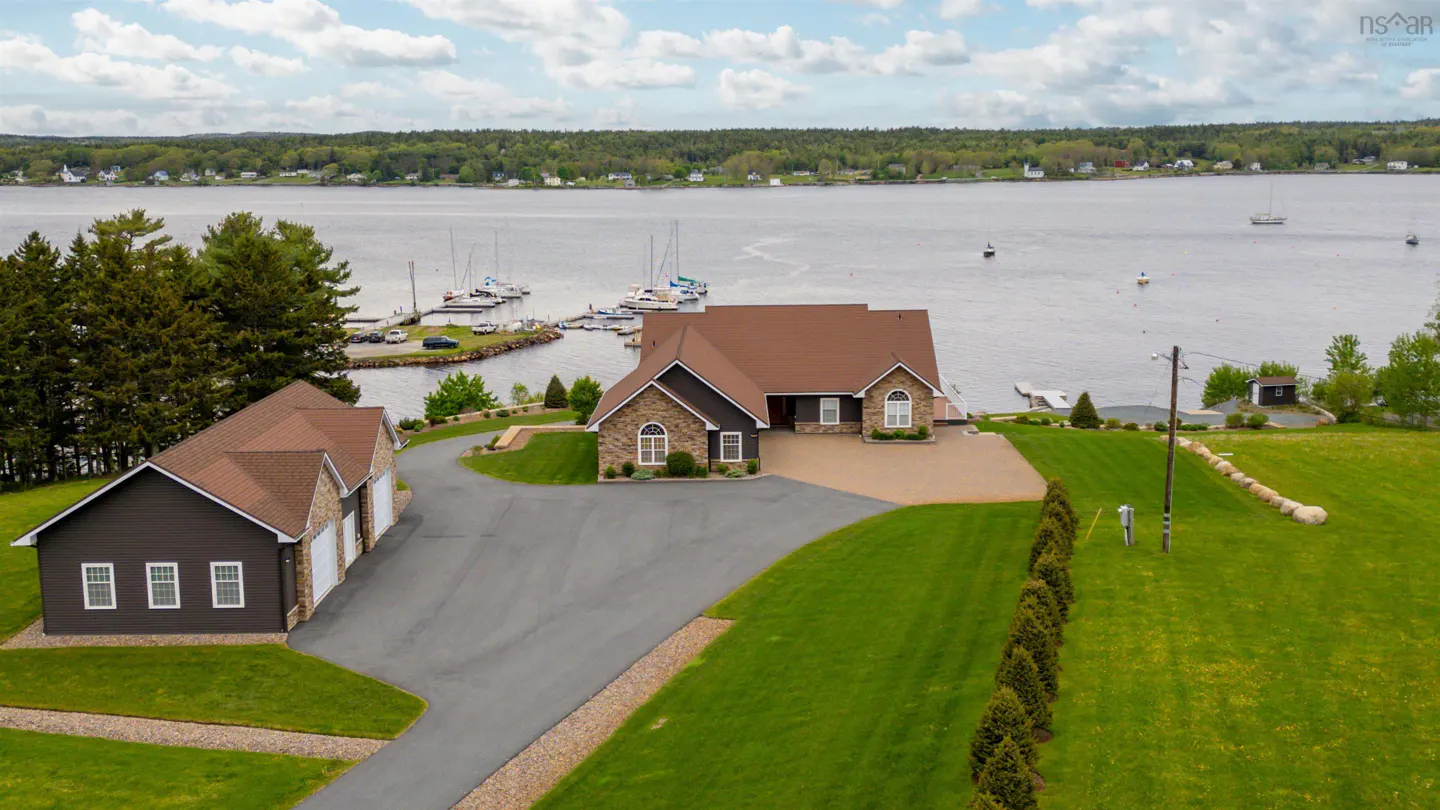 Aerial view of a brown house with a three-car garage on a green lawn near a bay with boats.