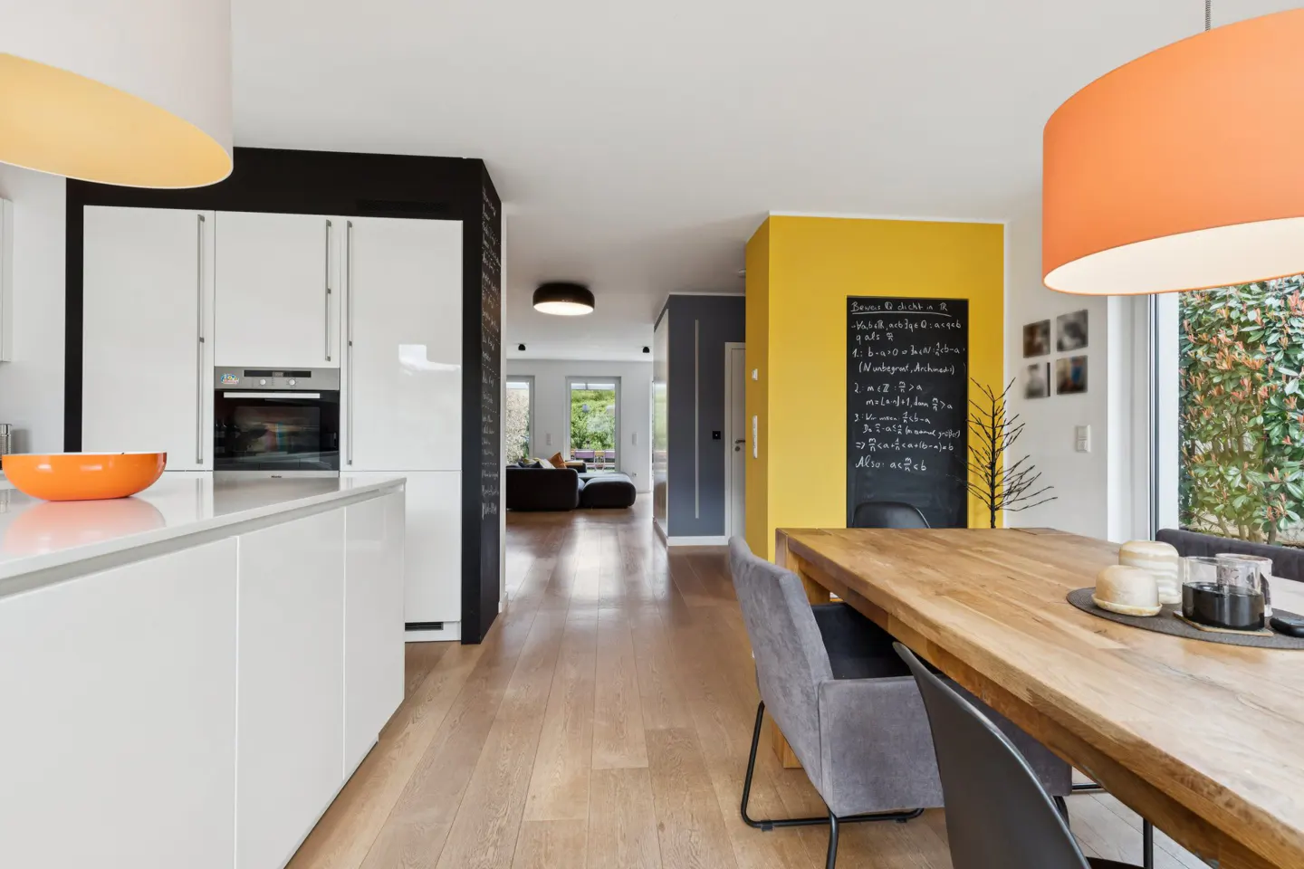 Bright, modern home interior with white cabinets, wood floors, and a dining area with a yellow wall and chalkboard.
