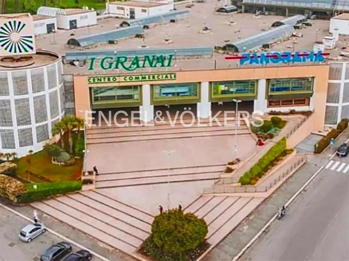 Aerial view of the I Granai shopping center with the Engel & Volkers logo in the foreground. Cars and people are visible.