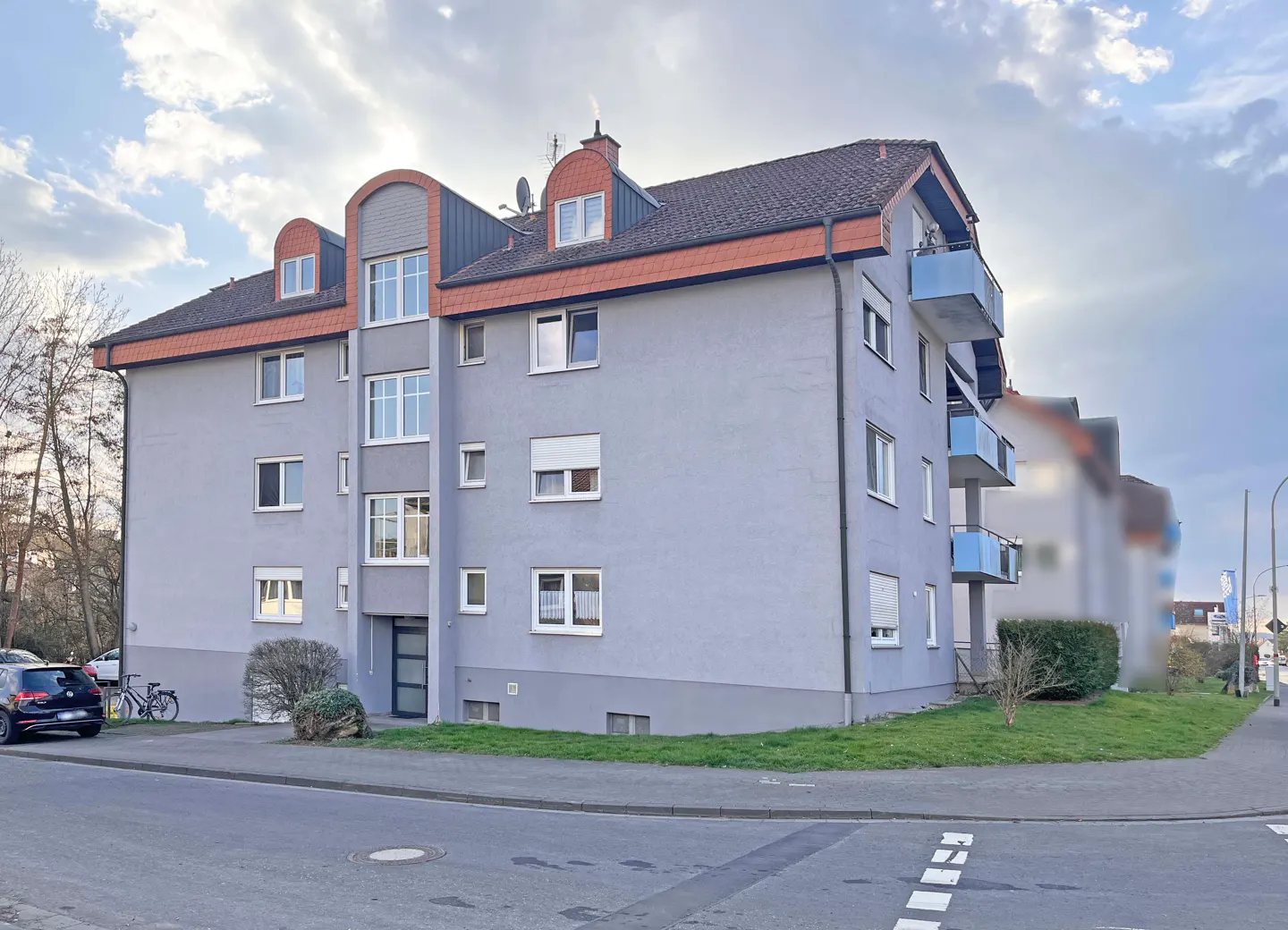 Exterior view of a three-story gray apartment building with blue balconies and a brown roof.