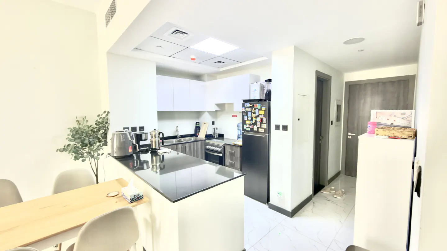 A bright, modern kitchen with white cabinets, black countertops, and a black refrigerator. A wooden table with chairs is in the foreground.