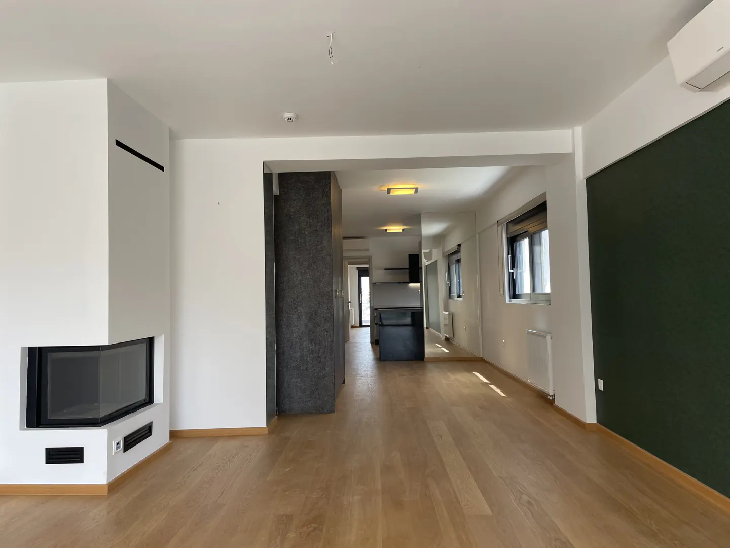 Bright, empty apartment with wood floors, white walls, and a modern fireplace. A dark green accent wall is visible.