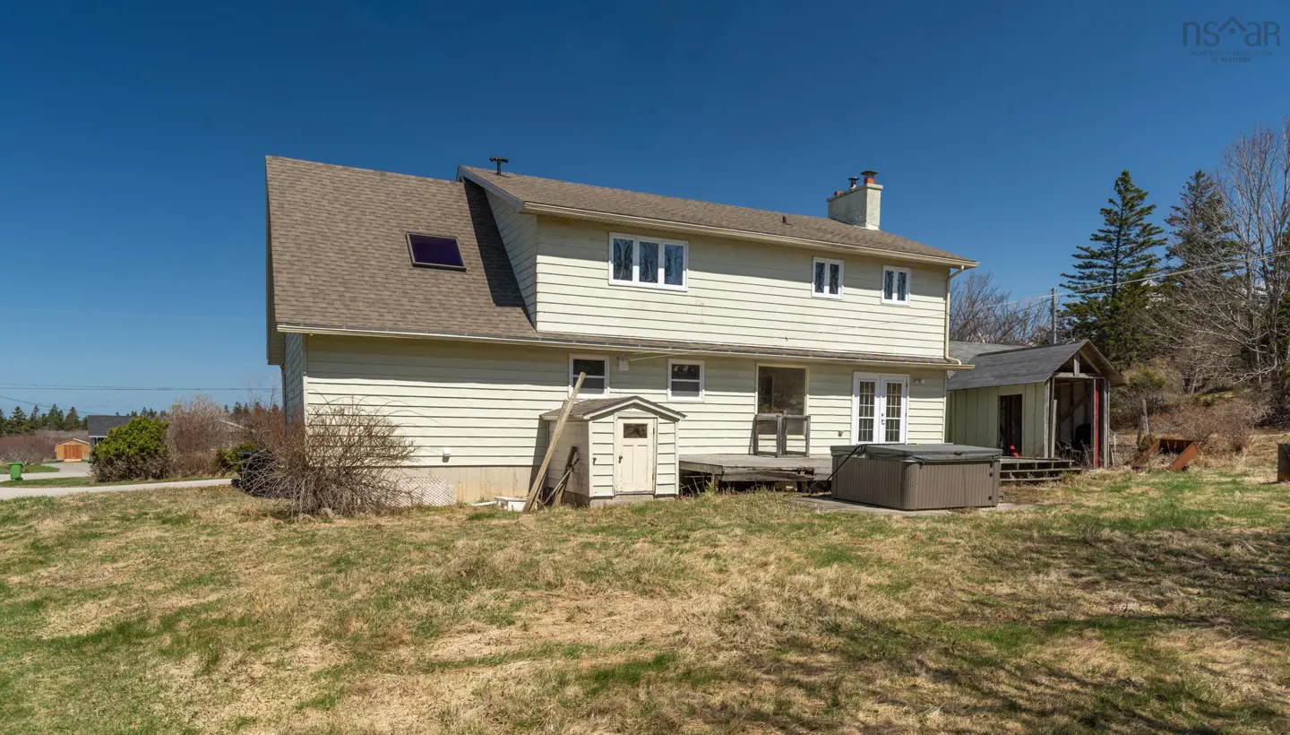 Backyard view of a two-story house with a brown roof, light yellow siding, a hot tub, and a small shed.