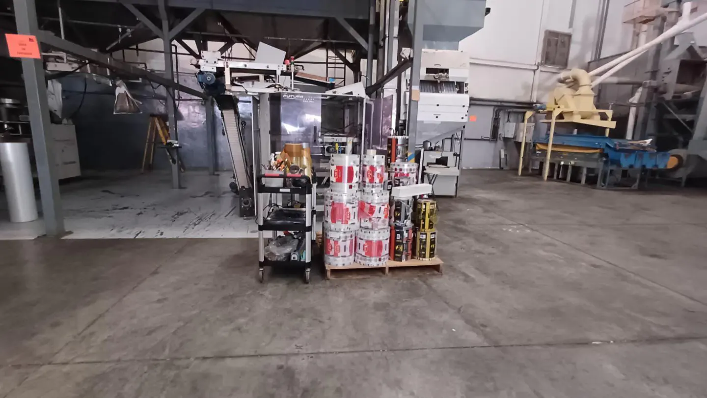 Industrial space with machinery, a cart, and stacked rolls of printed plastic film on a pallet.