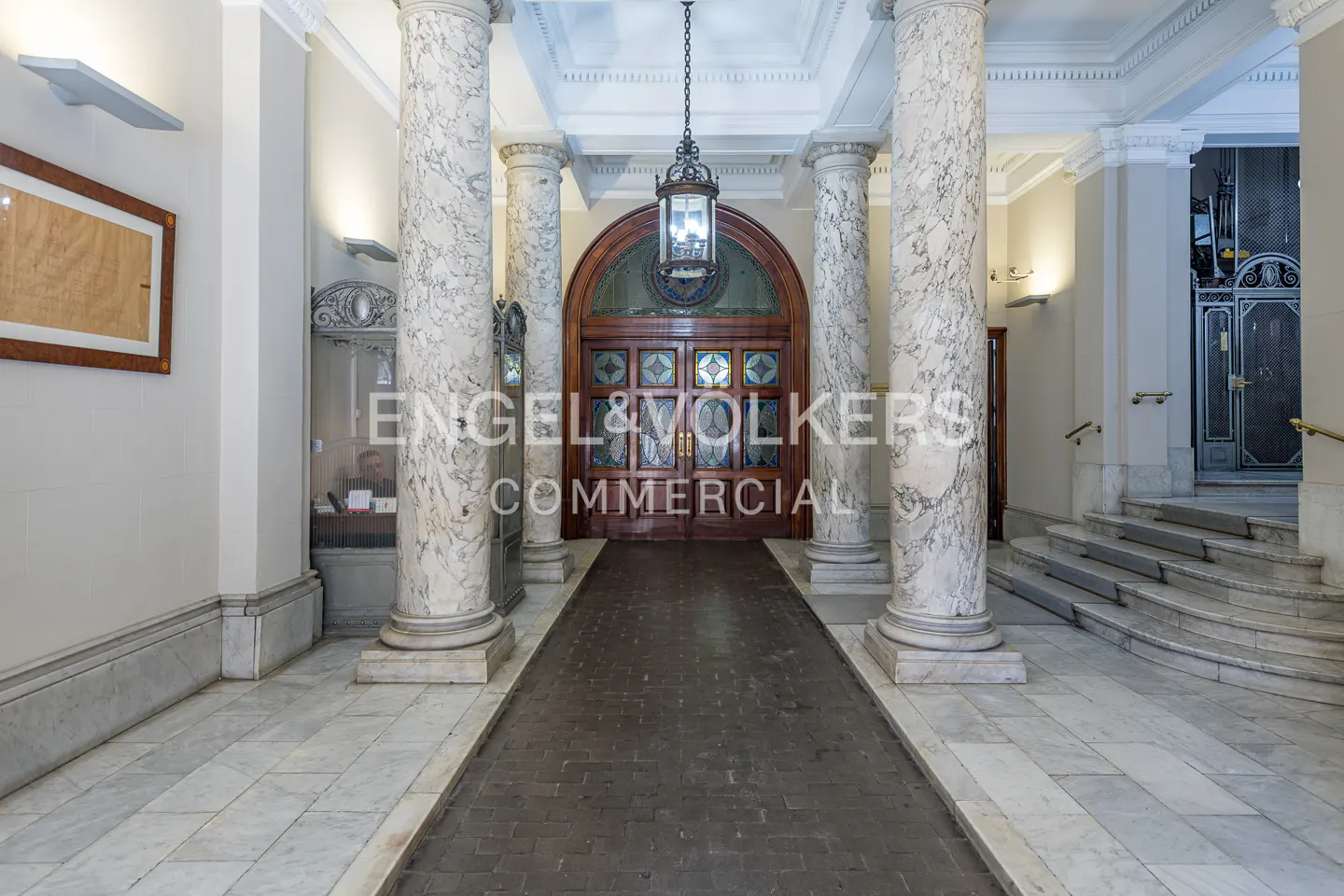 Grand entrance hall with marble columns, a dark wood door with glass panels, and a hanging lantern.