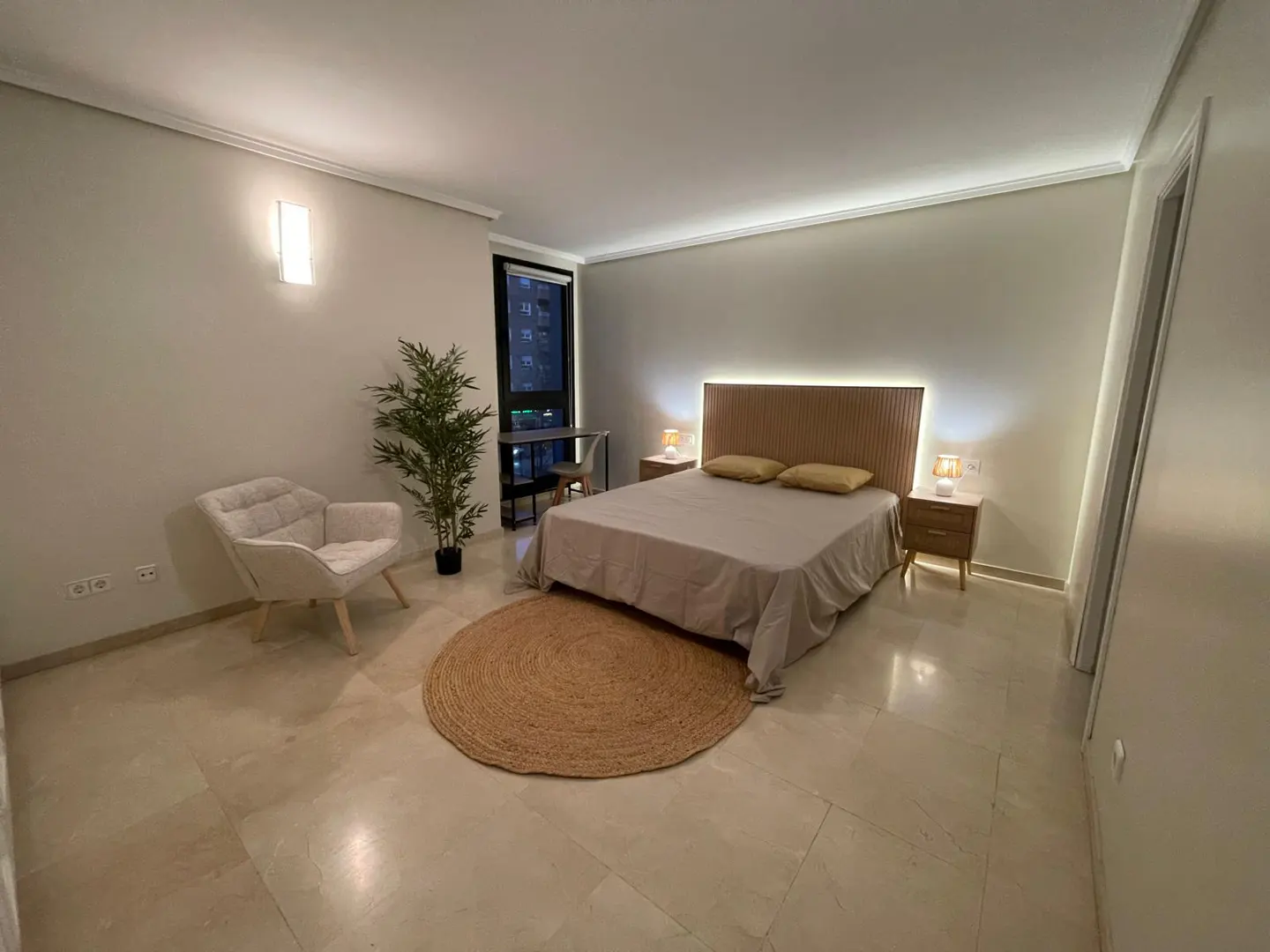 A modern bedroom with a bed, nightstands, a chair, and a round rug on a marble floor.
