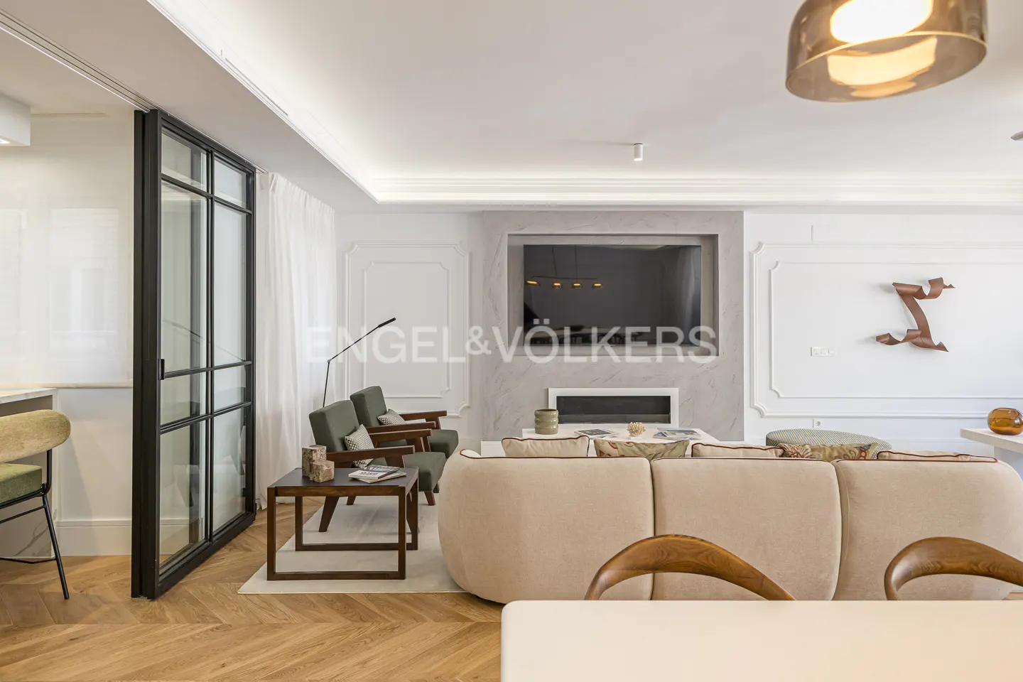Living room with beige sofa, green chairs, and a black-framed glass door. A TV is mounted above a modern fireplace.