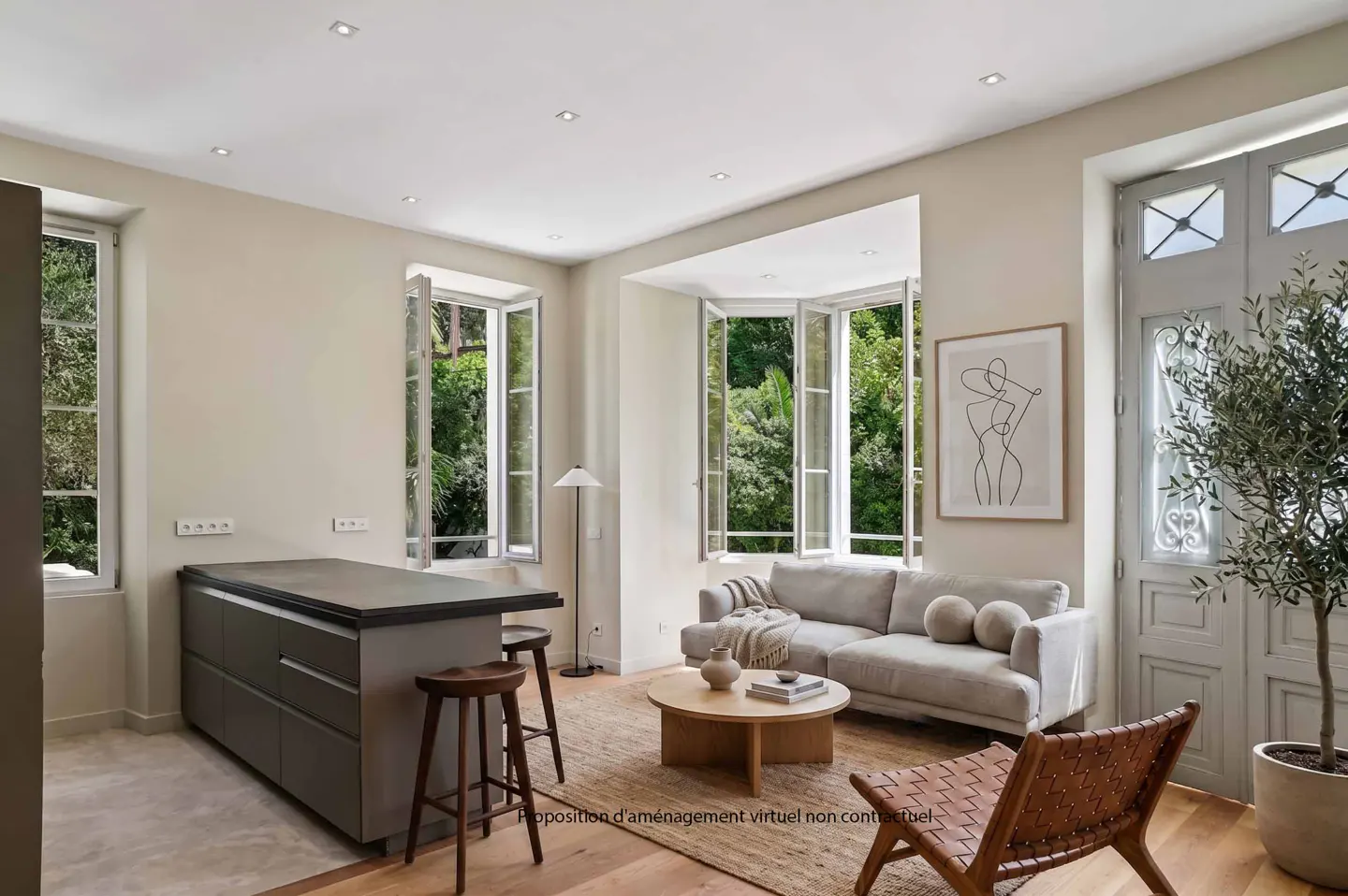 A bright living space with a gray kitchen island, wooden stools, a beige sofa, and a woven chair on a jute rug. Windows show green trees.