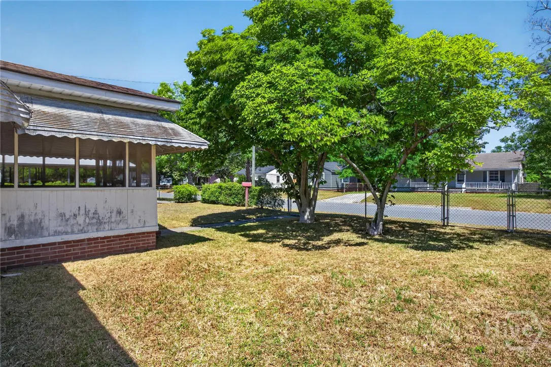 Exterior view of a house with a screened porch, lawn, and trees on a sunny day.