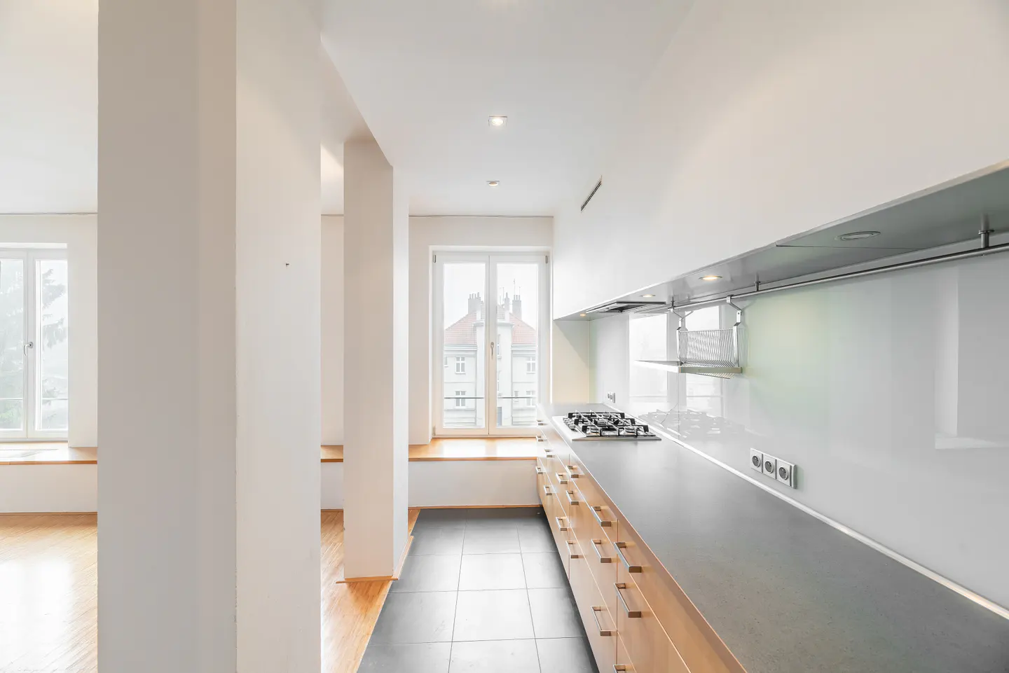 Bright, modern kitchen with light wood cabinets, gray countertops, and a gas stovetop. White walls and a window with a view.