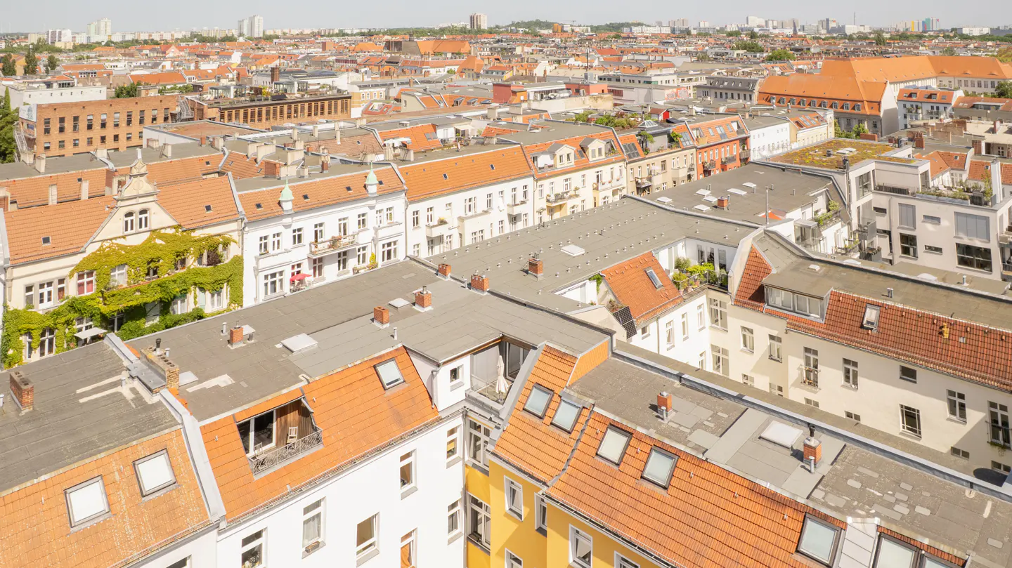 High-angle view of a dense European city neighborhood with terracotta-tiled roofs, white buildings, and lush greenery.