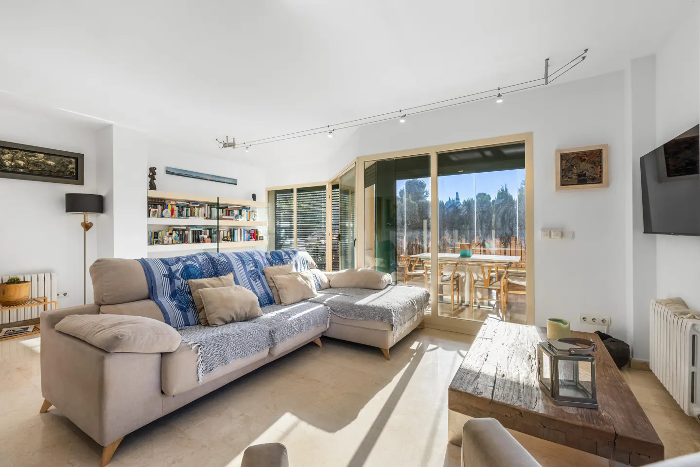 Bright living room with a beige sectional sofa, a rustic wood coffee table, and a view of an outdoor patio through sliding glass doors.
