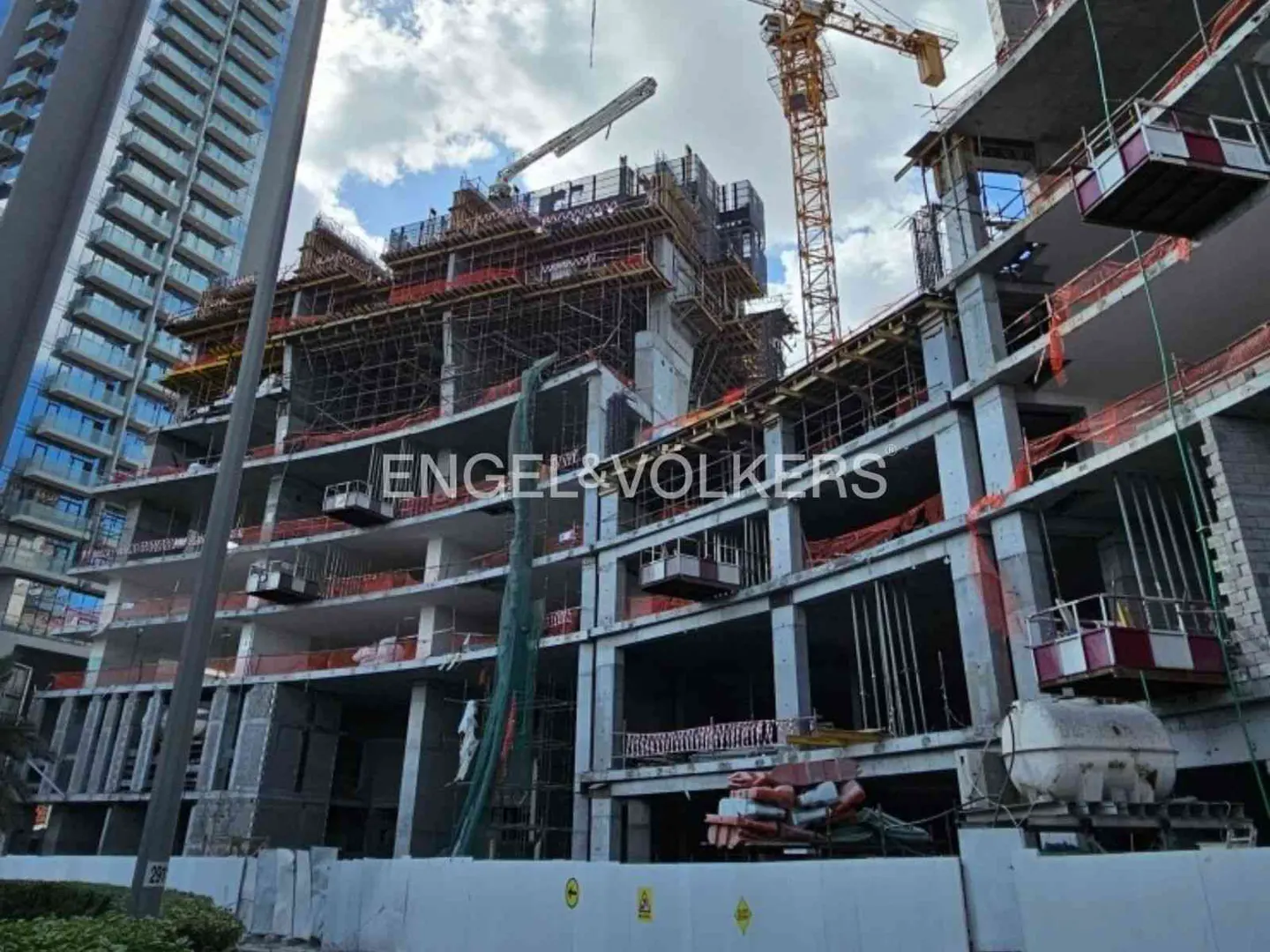 Construction site with a crane, scaffolding, and a partially built concrete building under a cloudy sky.