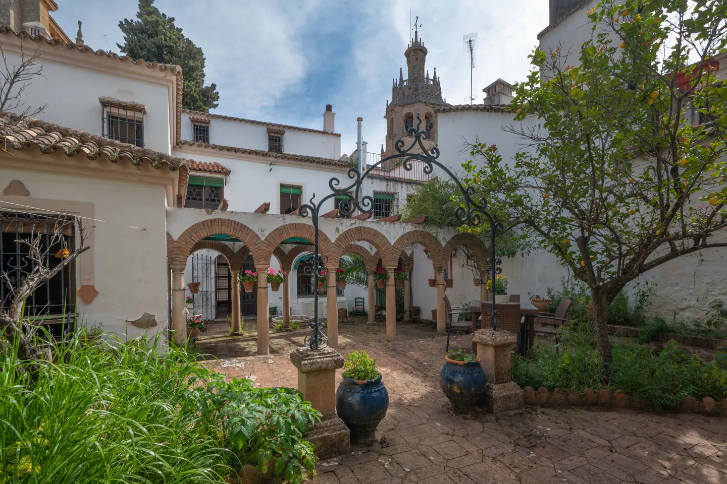 Courtyard with brick arches, potted plants, and a well. White buildings and a church tower are in the background.