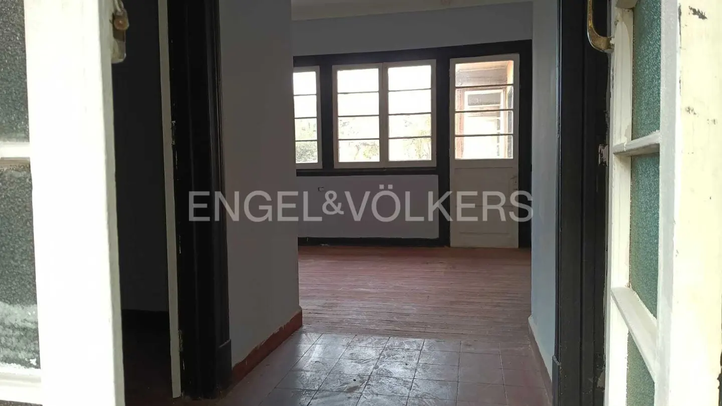 Interior view through a doorway into a room with multiple windows and the Engel & Völkers logo.