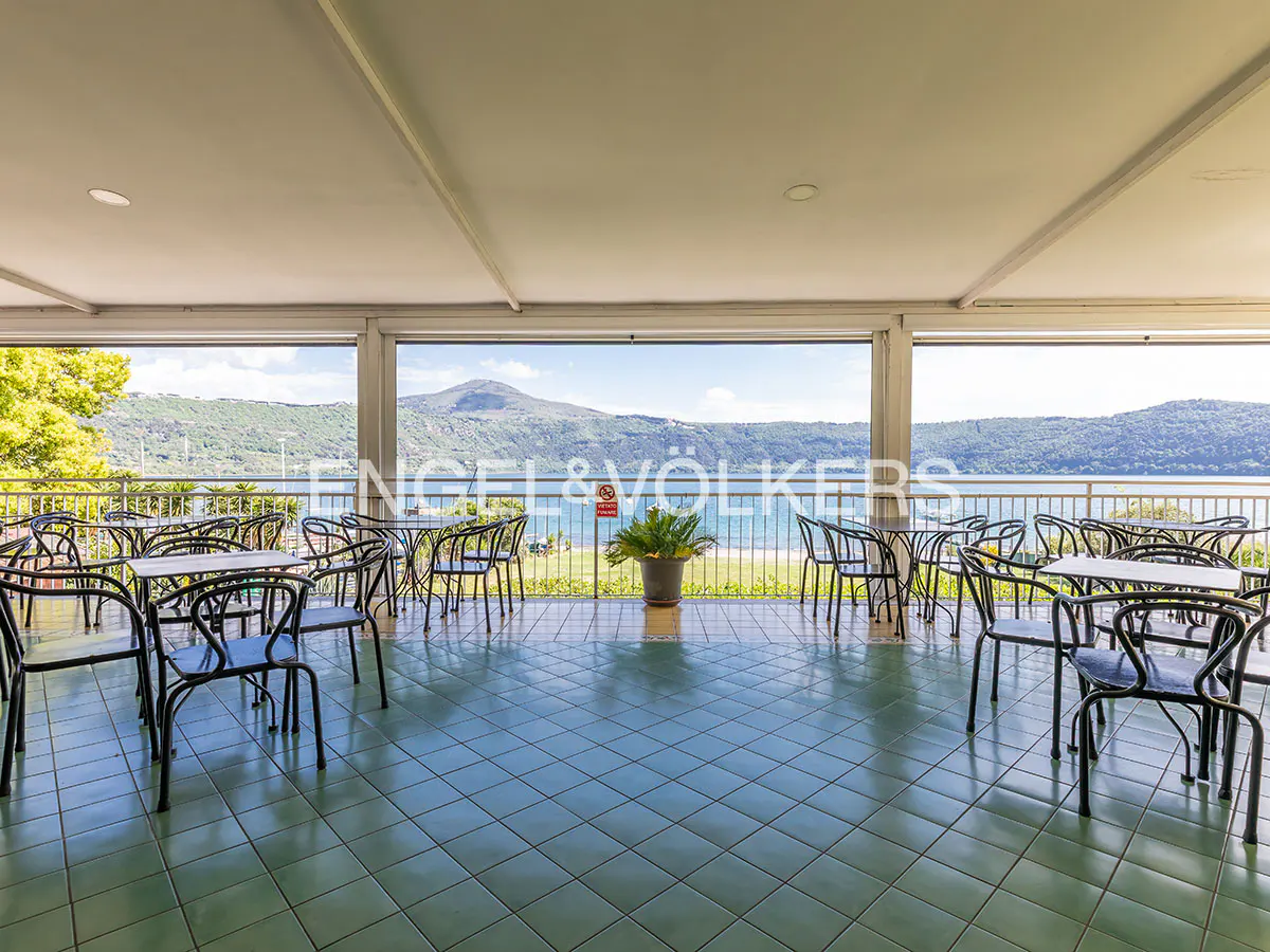 Outdoor patio with black chairs and tables on a green tiled floor overlooking a lake and mountains.