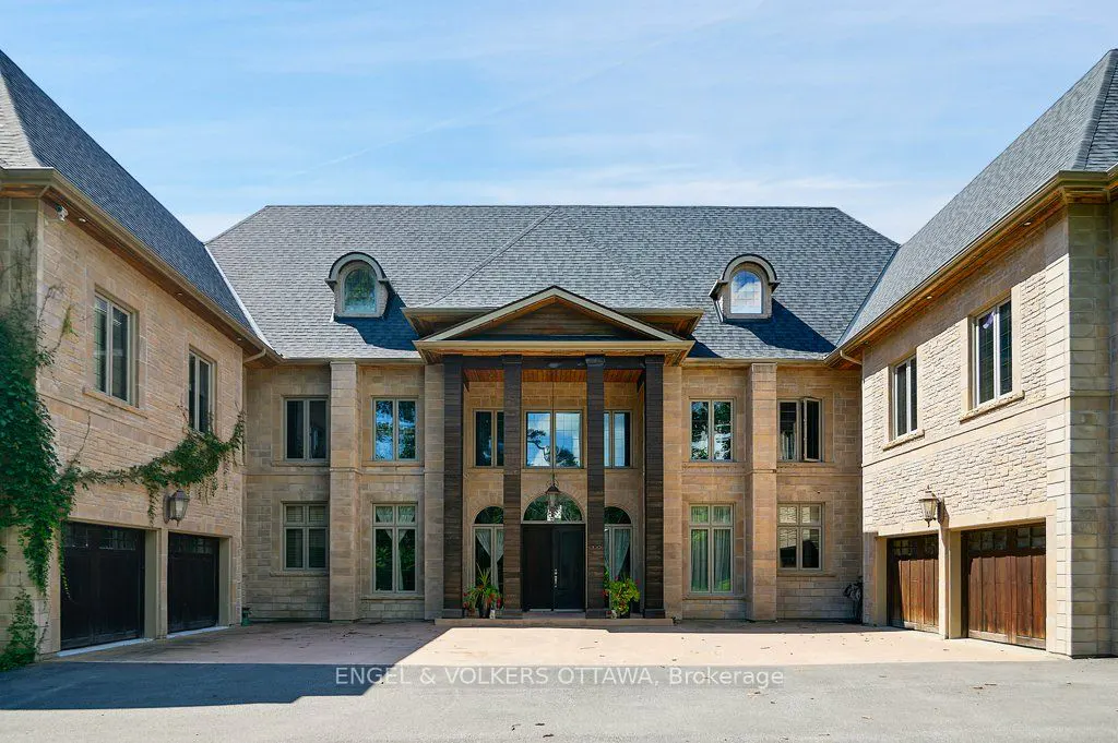Front view of a large, symmetrical stone house with dark wood columns and a gray roof under a blue sky.