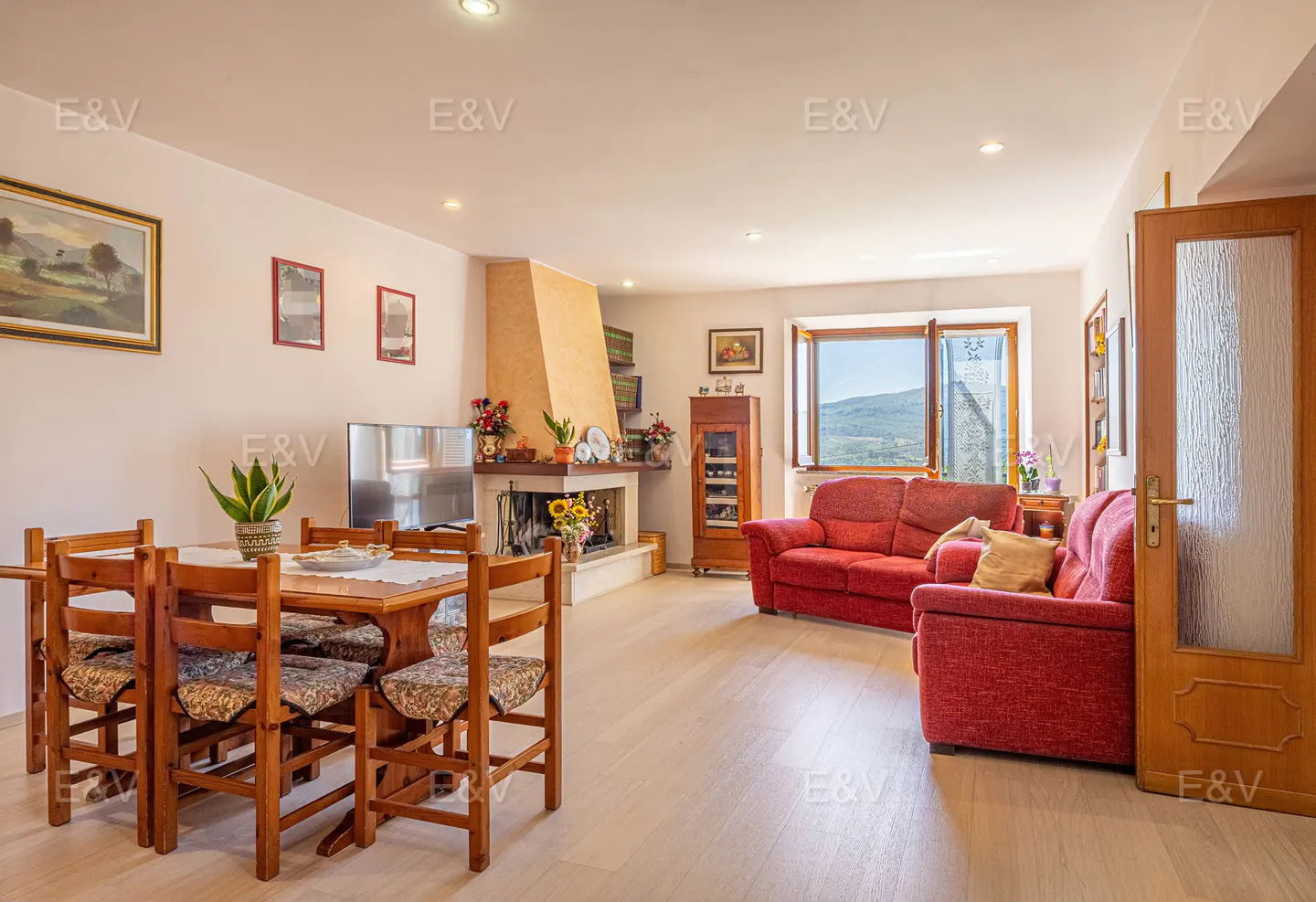 Living room with a wooden table, red sofa, fireplace, and a view from the window.