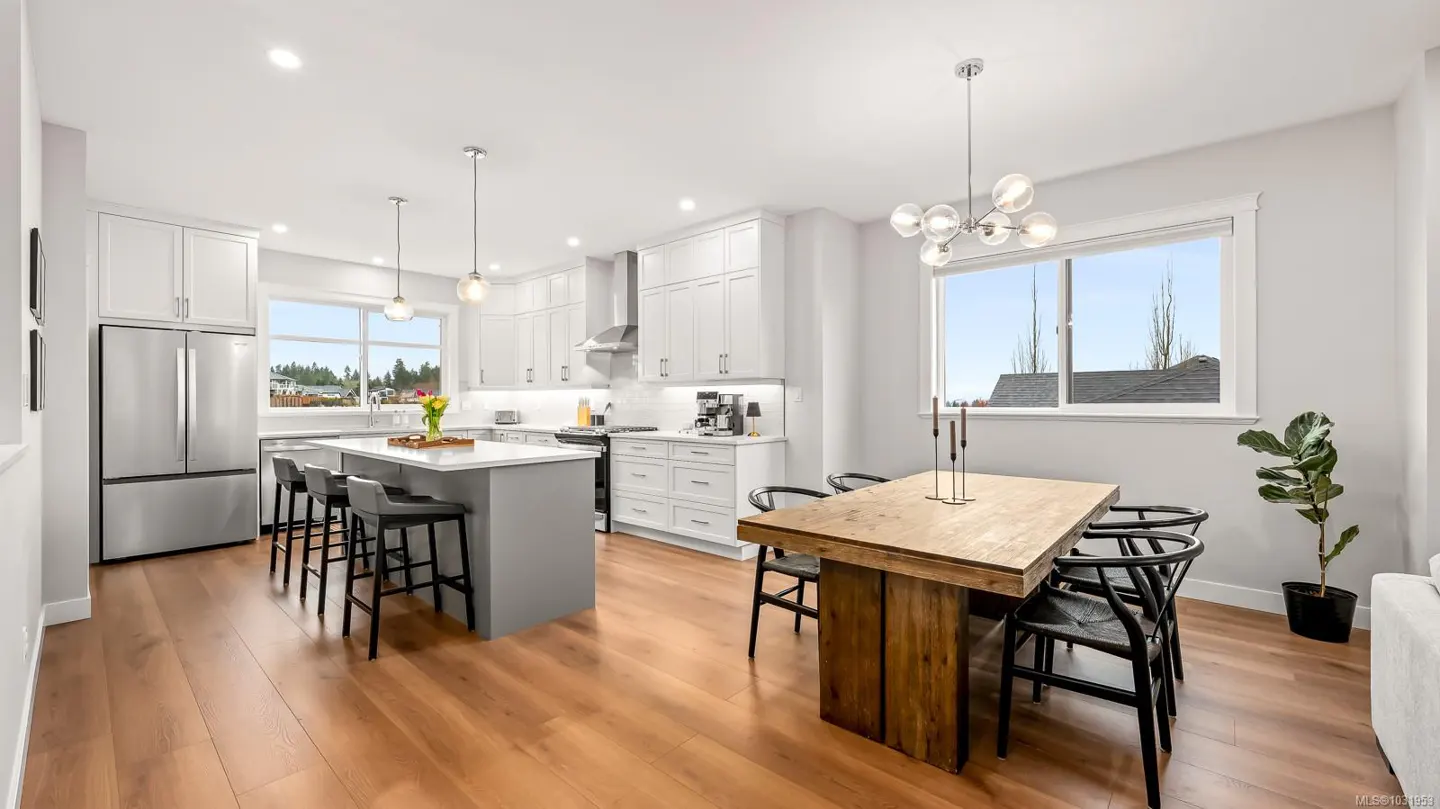 Bright, modern kitchen with white cabinets, stainless steel appliances, and a gray island with bar stools. A wooden dining table sits nearby.
