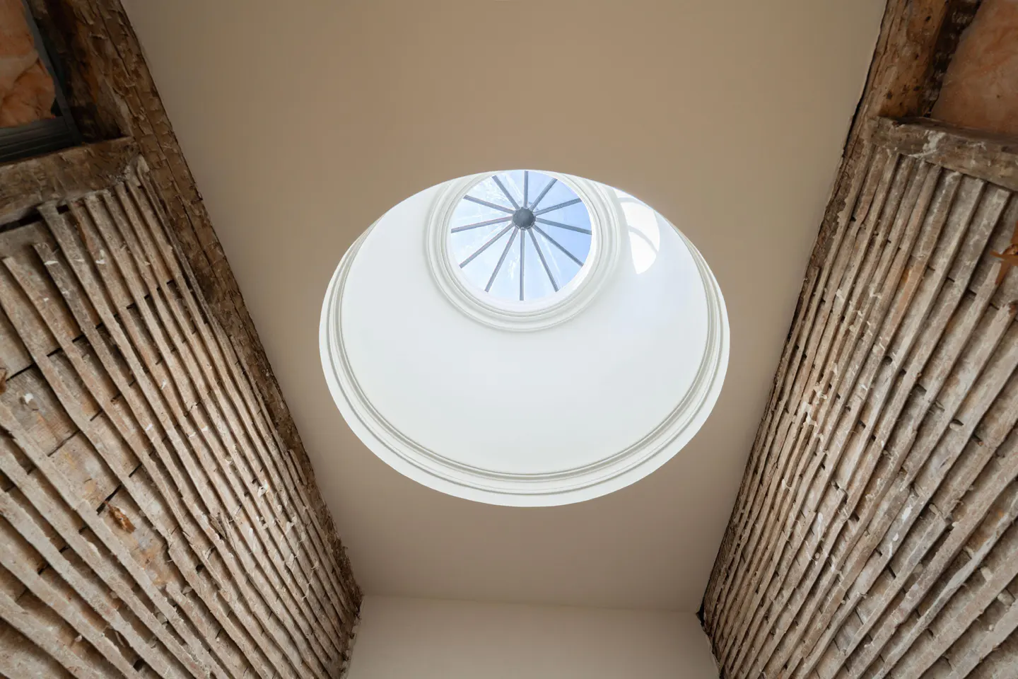 Looking up at a round skylight with a view of the blue sky, framed by exposed wood beams.