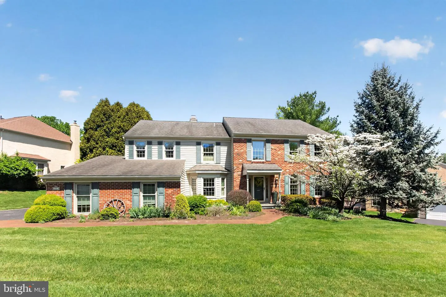 Two-story house with brick and siding, green shutters, and a large lawn under a blue sky.