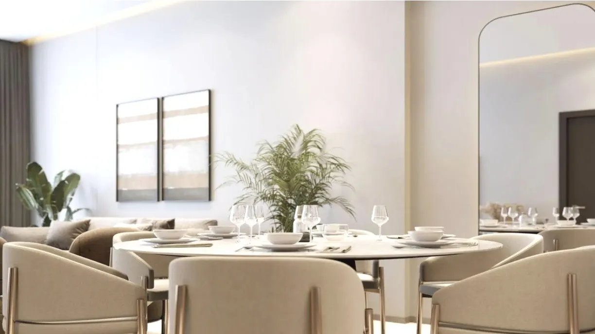 A bright dining area with a round table set for a meal, surrounded by beige chairs with gold accents. A plant sits in the center, with artwork and a mirror in the background.
