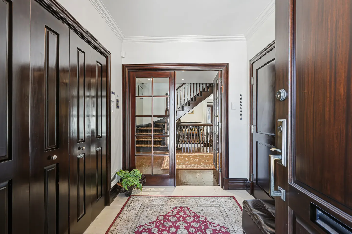 A home's entryway with dark wood doors, a patterned rug, and a view of the staircase through glass doors.