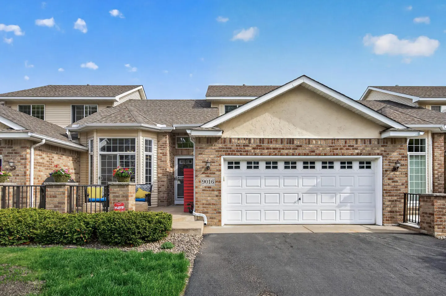 Exterior view of a brick townhouse with a white garage door and a red front door.