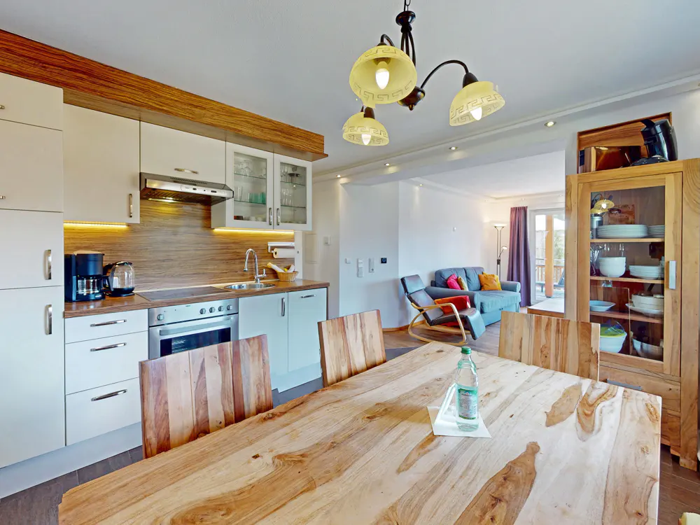 A bright, open-concept kitchen and dining area with a wooden table, white cabinets, and a view into the living room.
