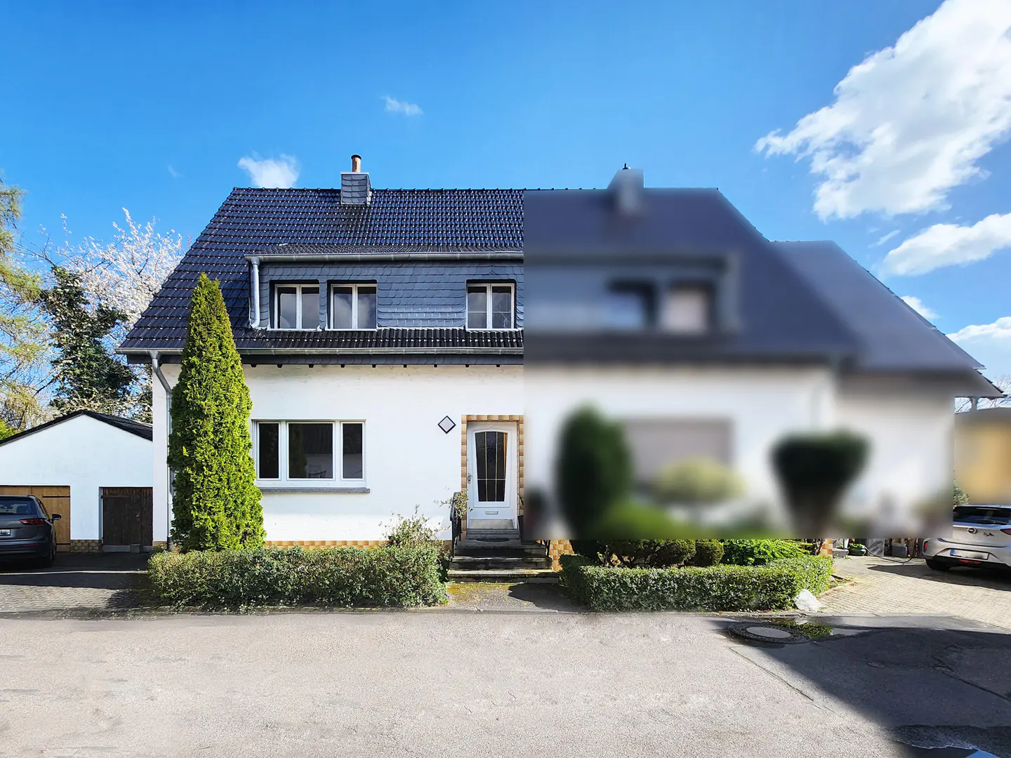 Two-story white house with a dark blue roof, green bushes, and a blue sky. The right side of the image is blurred.