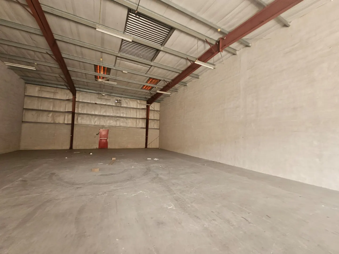 An empty warehouse with a concrete floor, metal beams, and a red door in the back.