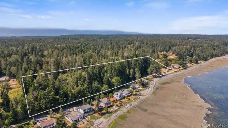 Aerial view of a wooded lot outlined in white, adjacent to a beach with houses and the ocean.