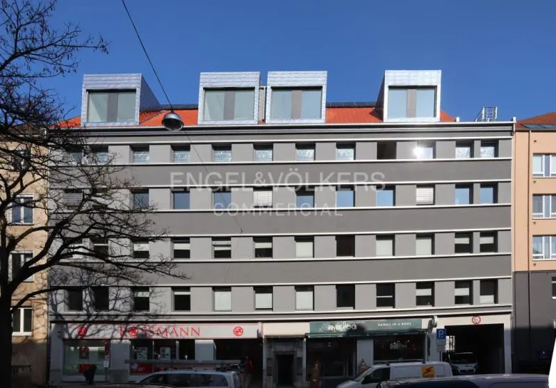 Exterior of a gray, multi-story commercial building with retail shops on the ground floor. Engel & Völkers logo is visible.