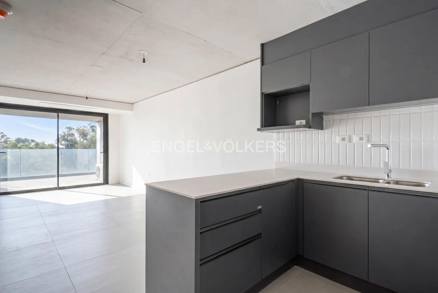 Modern kitchen with dark grey cabinets, white tiled backsplash, and a sliding glass door leading to a bright balcony.