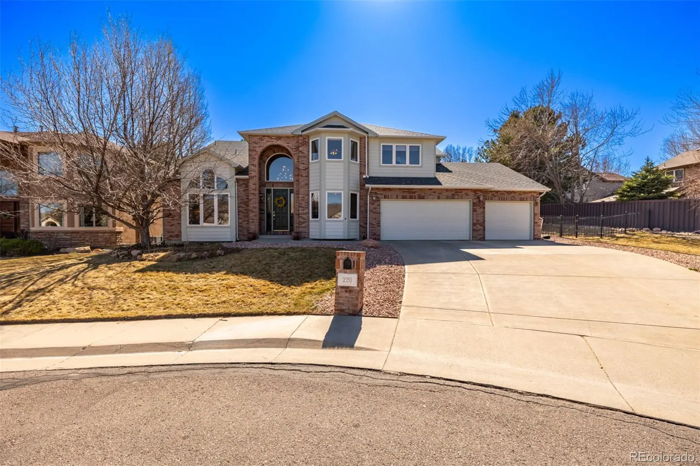 Two-story house with brick and light gray siding, a three-car garage, and a large driveway on a sunny day.