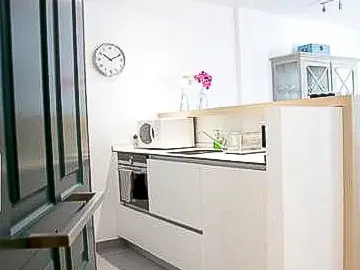 A bright kitchen with white cabinets, a microwave, and an oven. A clock hangs on the white wall, and a green door is partially visible.